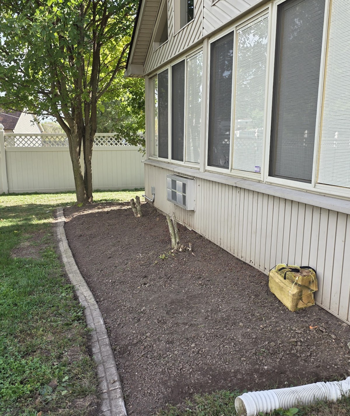 A planting bed freshly cleared with small tree stumps cut down, ready for mulch